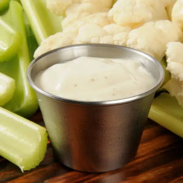 Ranch dressing in a metal sauce bowl surrounded by vegetables