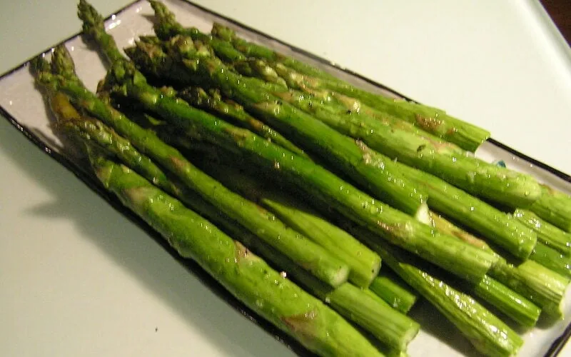 Roasted asparagus with bacon and garlic laying on a white plate