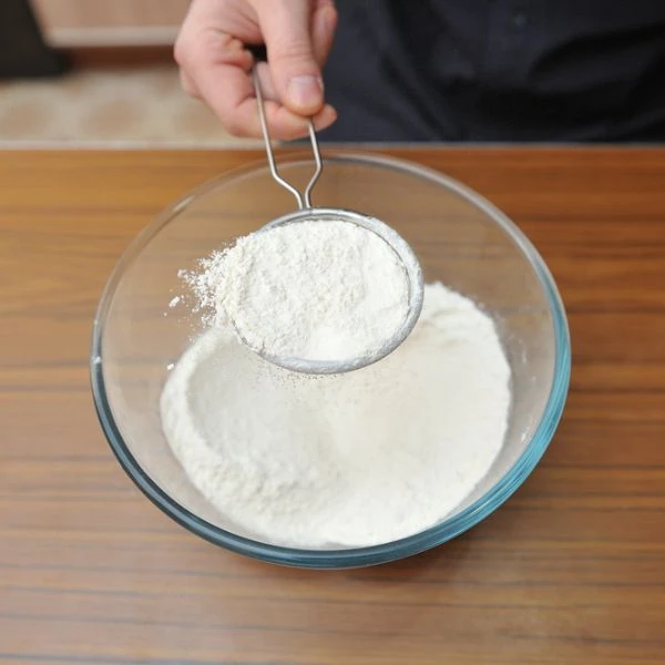 Sifting powdered sugar into a glass bowl