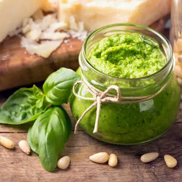A jar of open pesto with pine nuts around it