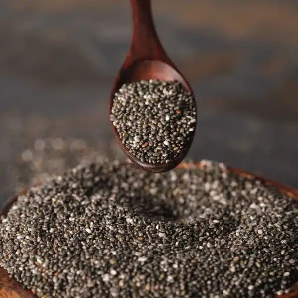 Chia seeds being poured in a wooden bowl from a wooden spoon