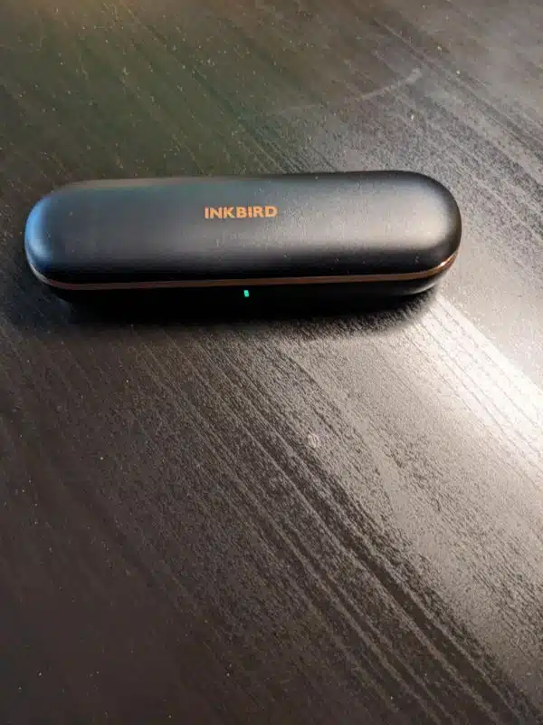 Charging case of the INKBIRD INT-11P-B being shown with a status light green showing it is fully charged